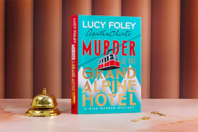 UK Copy of Lucy Foley's Miss Marple novel, Murder at the Grand Alpine, on a marble table with a hotel bell and room keys